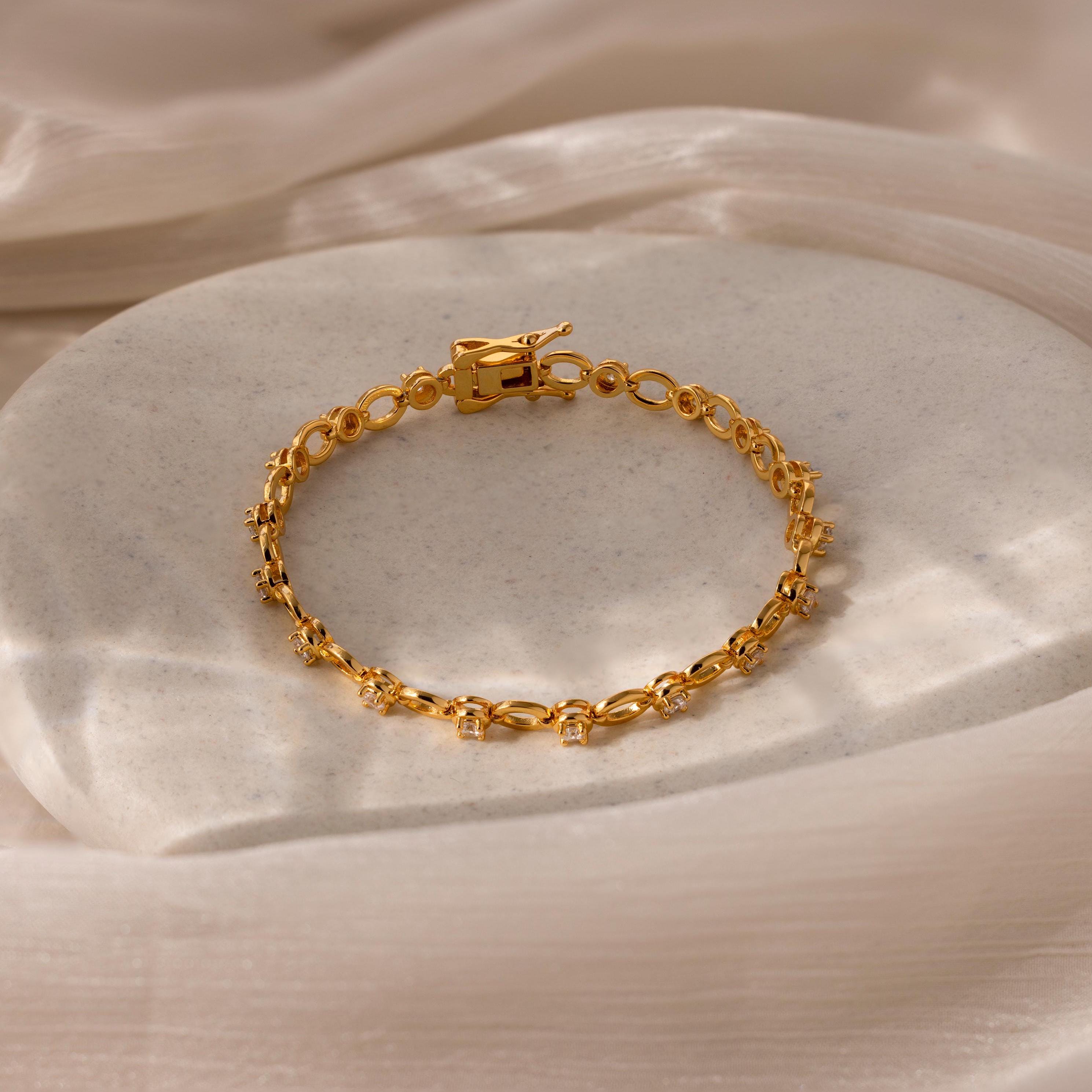 A gold chain tennis bracelet with sparkling stones, displayed on a silky surface.